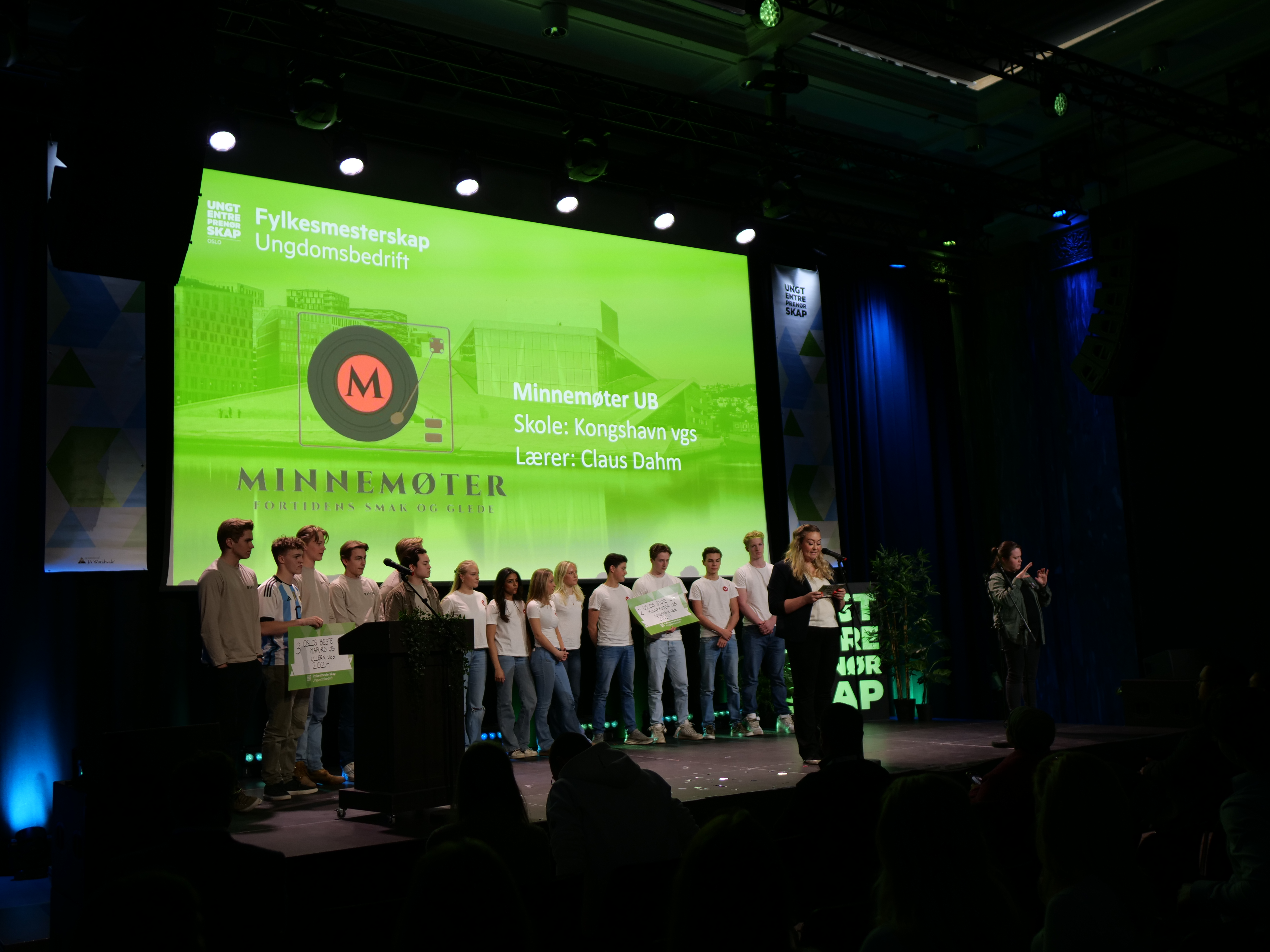 en gruppe mennesker som står på en scene med en stor skjerm bak seg