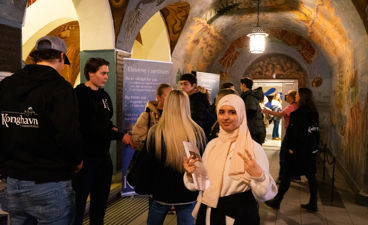 en gruppe mennesker som står i et rom med kunst på veggen