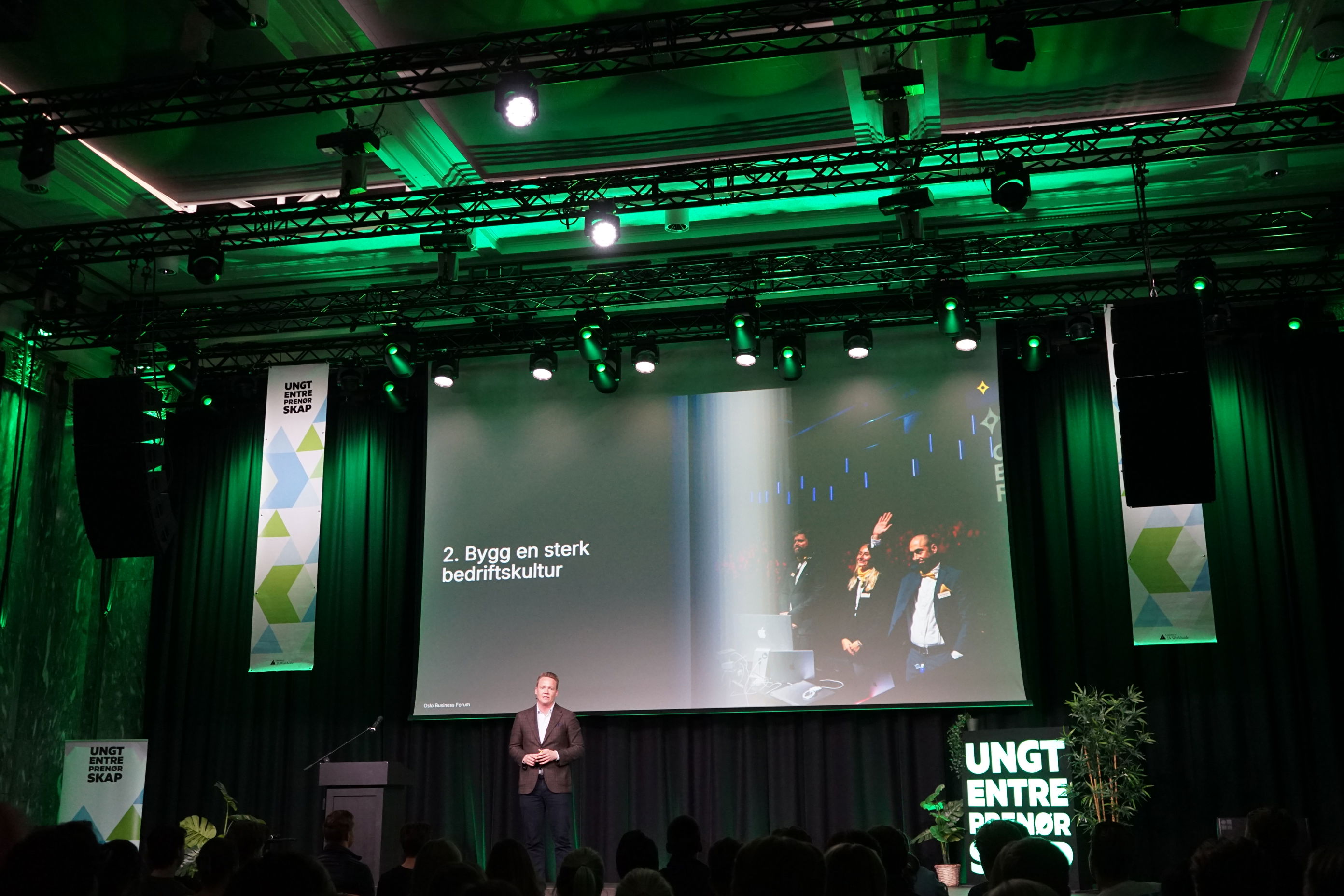 en person som står på en scene med en stor skjerm foran seg