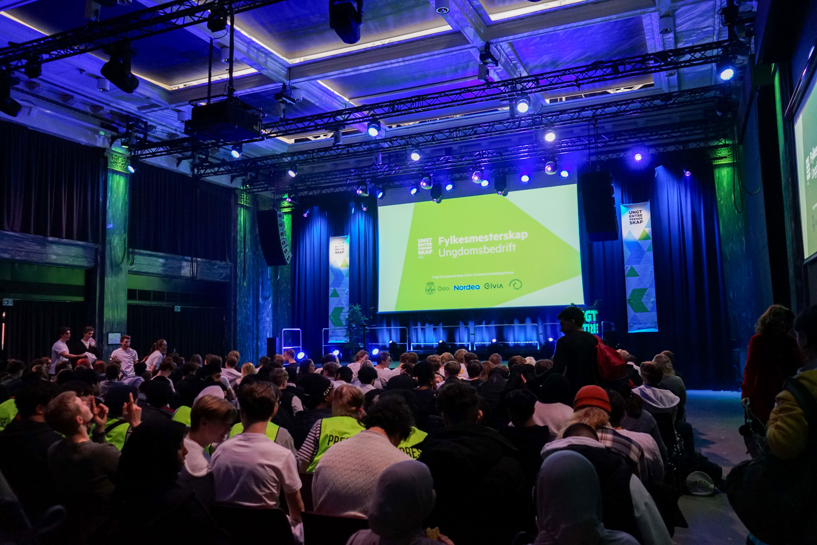 en gruppe mennesker som sitter i et rom med en stor skjerm en gruppe mennesker som sitter i et rom med en stor skjerm