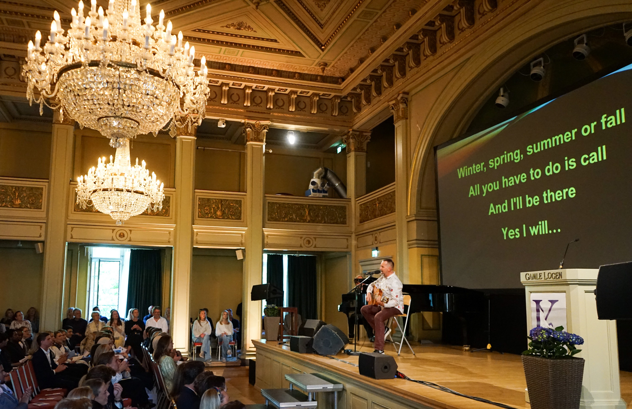 en person som spiller piano i et rom med en stor lysekrone