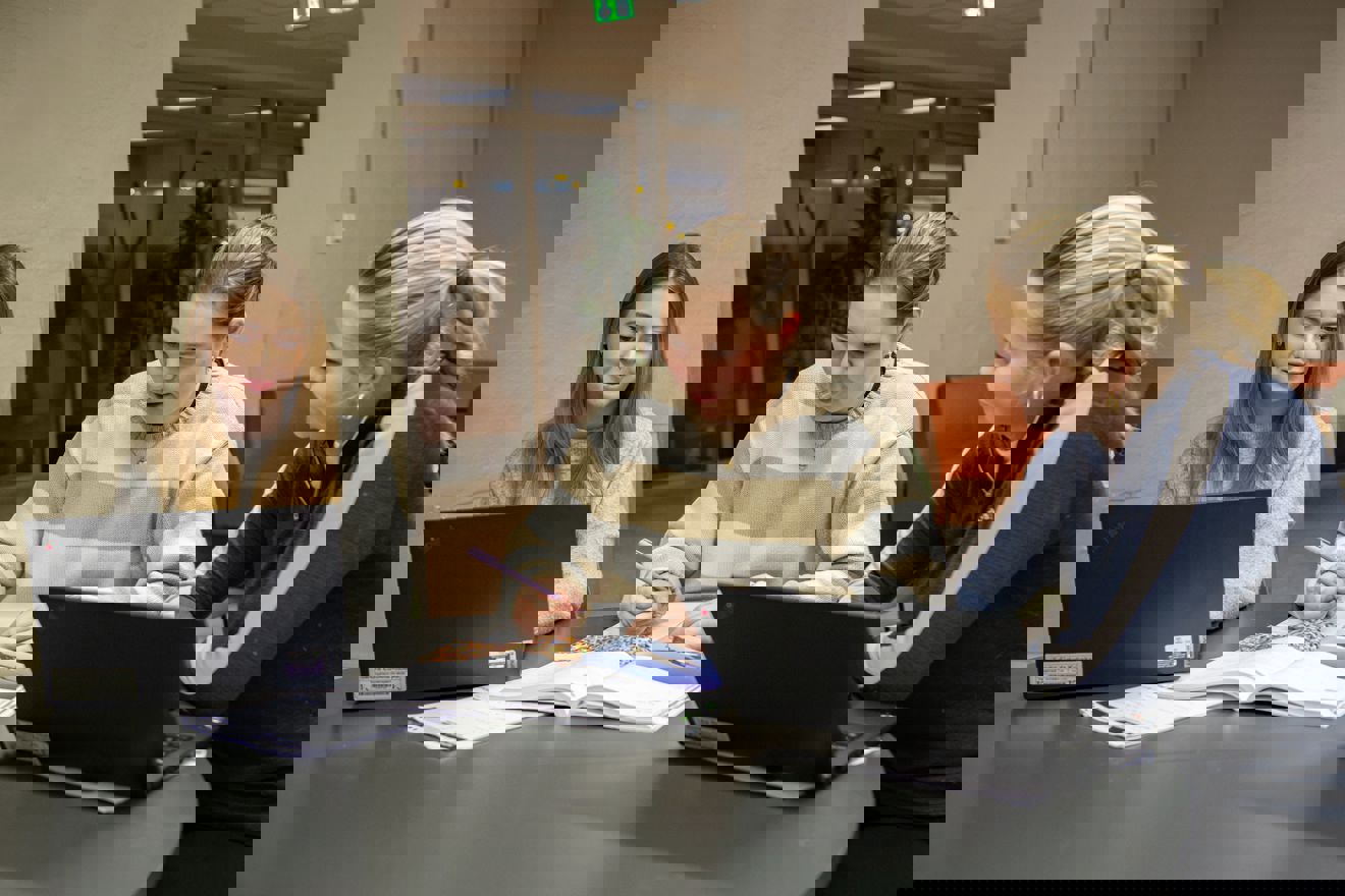 En gruppe personr som sitter ved et bord og ser på en bærbar datamaskin