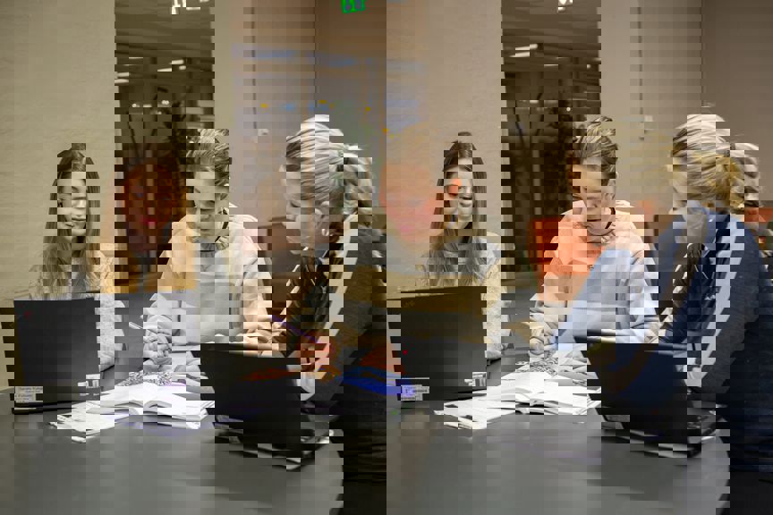 En gruppe personr som sitter ved et bord og ser på en bærbar datamaskin