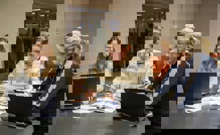 En gruppe personr som sitter ved et bord og ser på en bærbar datamaskin En gruppe personr som sitter ved et bord og ser på en bærbar datamaskin