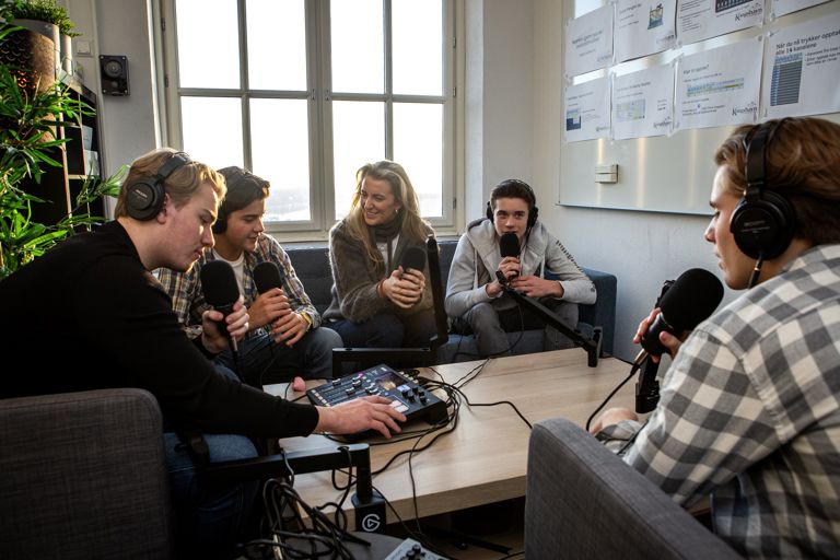 en gruppe mennesker som sitter rundt et bord med en person som står foran dem