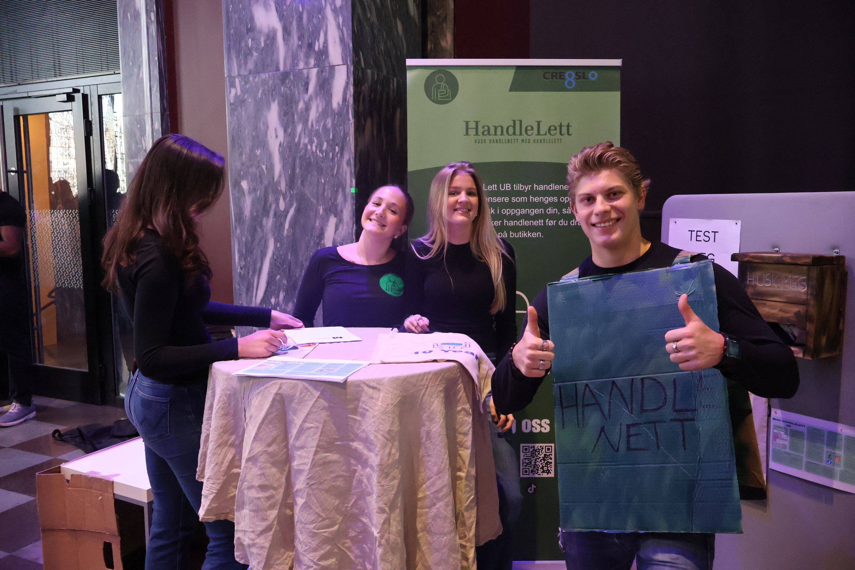 en gruppe mennesker som står rundt et bord med et skilt en gruppe mennesker som står rundt et bord med et skilt