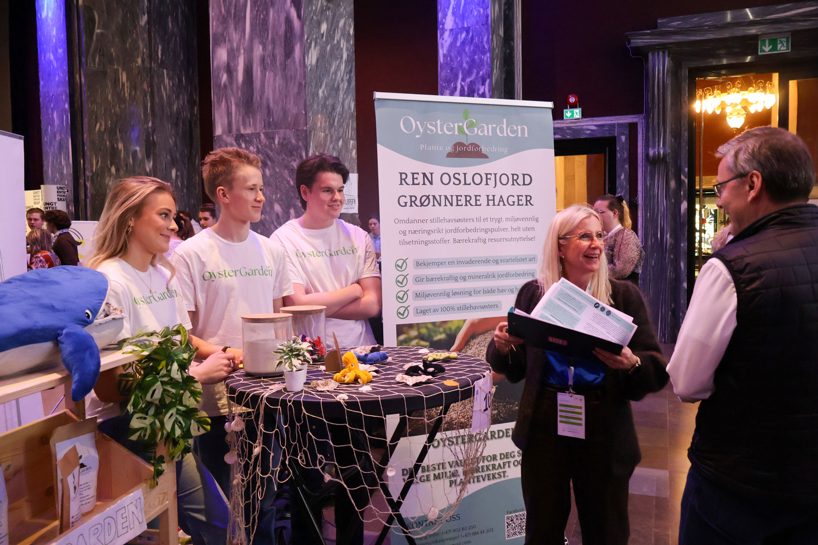 en gruppe mennesker som står rundt et bord med blomster og et skilt en gruppe mennesker som står rundt et bord med blomster og et skilt