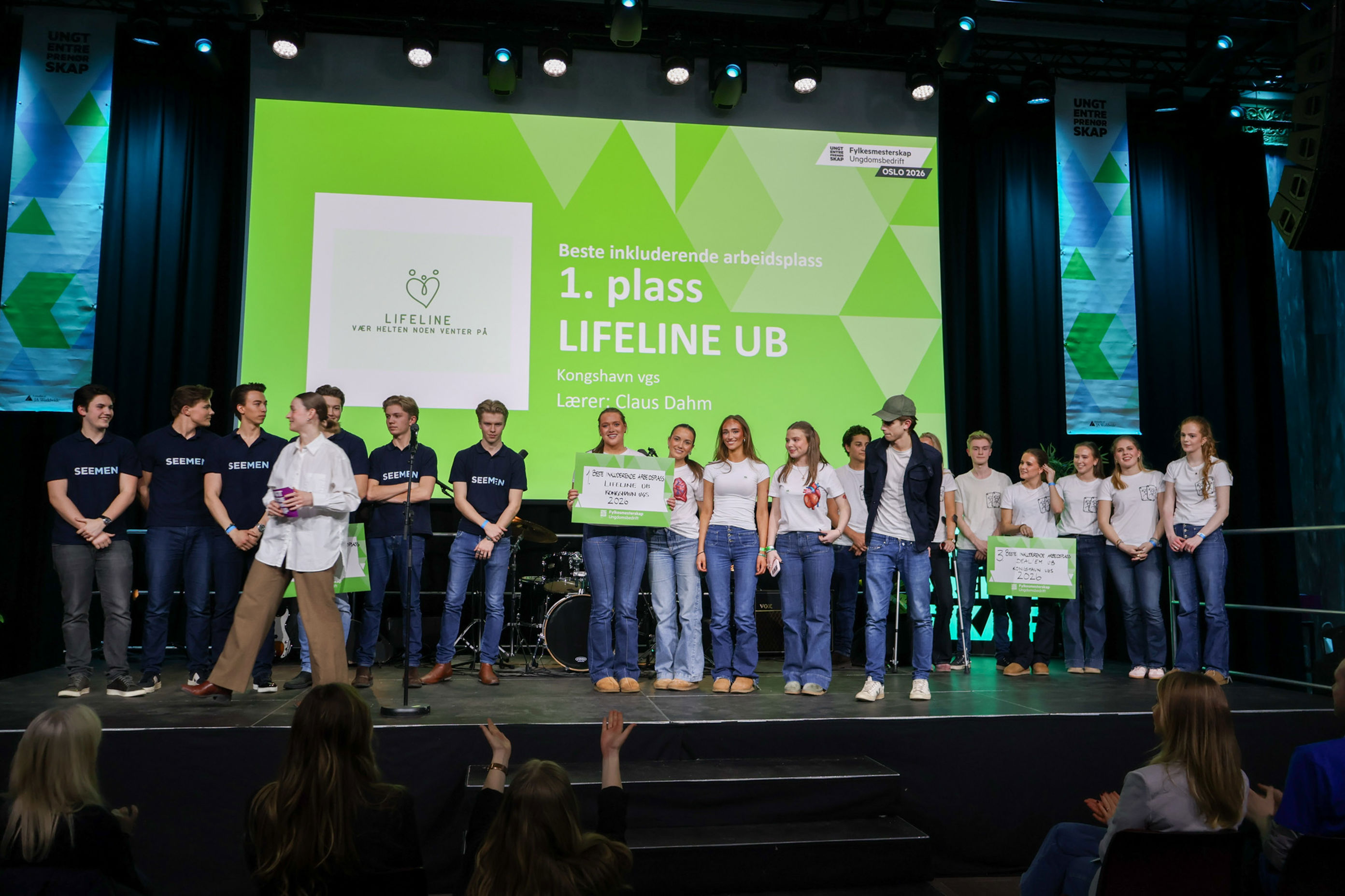 En gruppe mennesker som står på en scene med en green screen bak seg