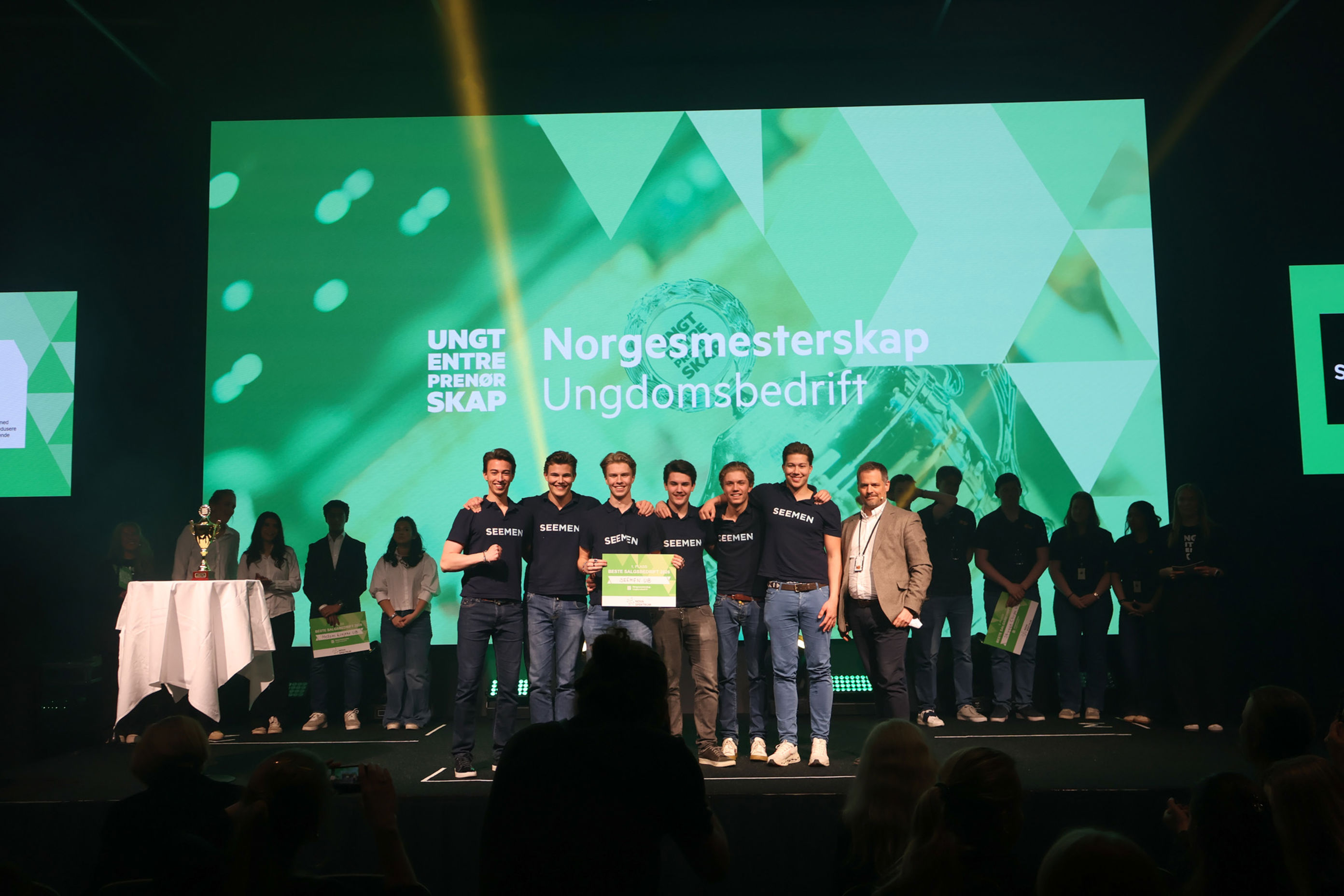 a group of people standing on a stage with a large screen behind them