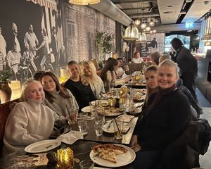 En gruppe personr som sitter ved et bord med pizza
