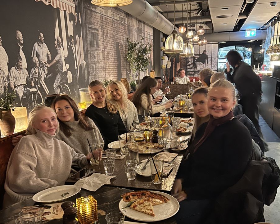 En gruppe personr som sitter ved et bord med pizza En gruppe personr som sitter ved et bord med pizza