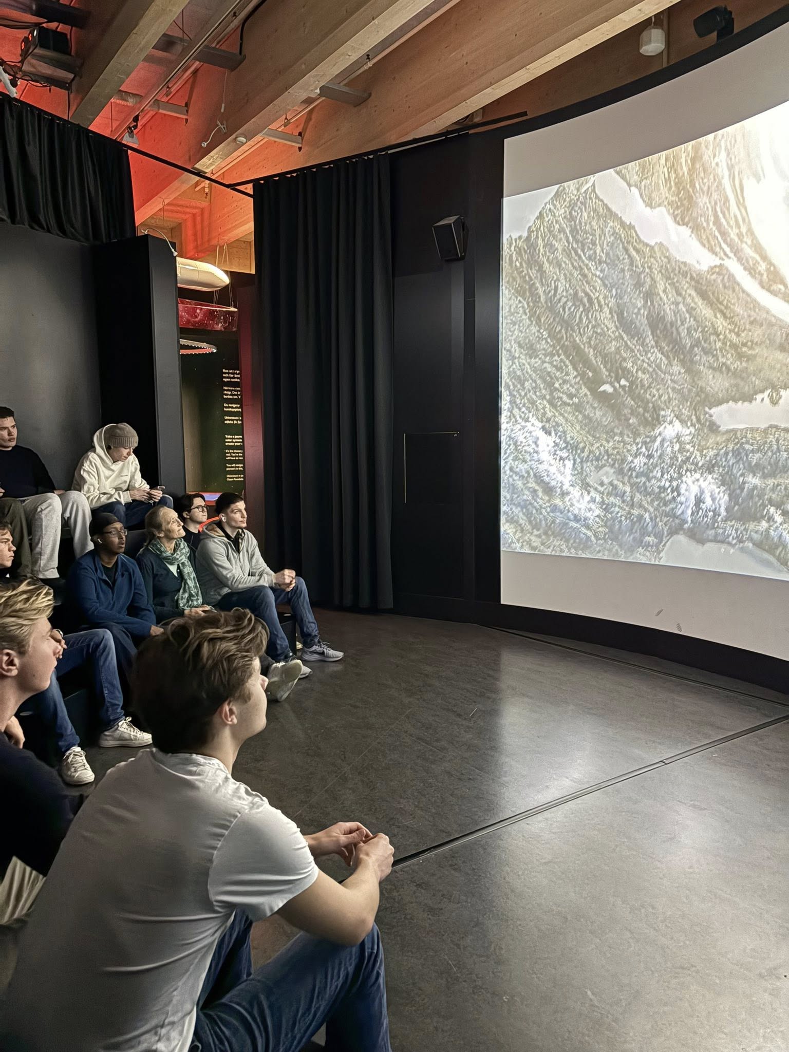 en gruppe mennesker som sitter i et rom med en stor skjerm