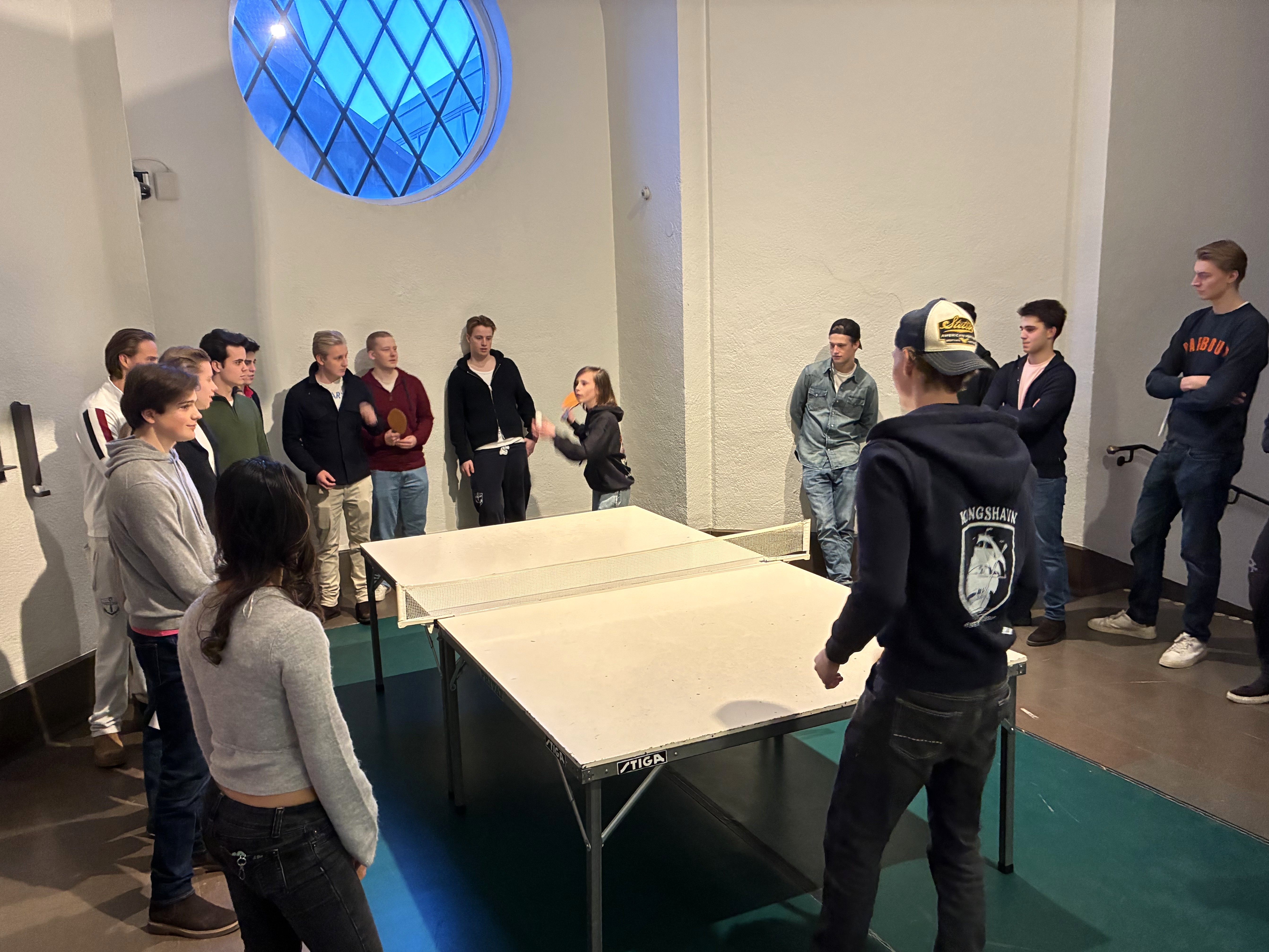 en gruppe mennesker som står rundt et bord med en person sittende ved det