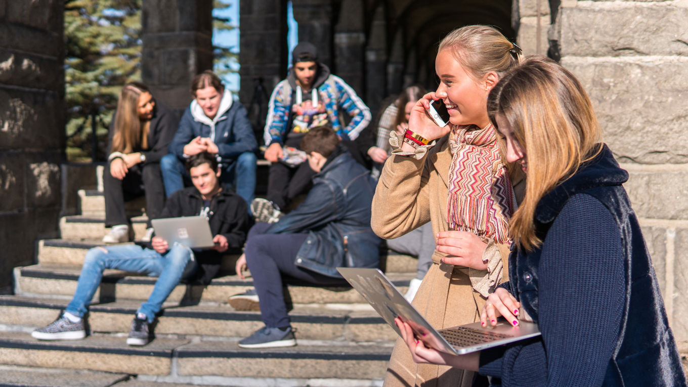 Foto: Elevgruppe En elev snakker i telefonen, andre elever prater