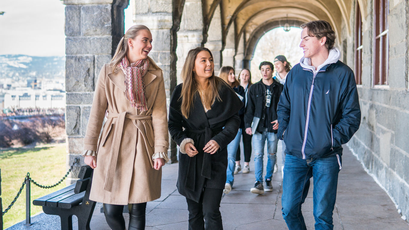 Tre elever i forgrunnen går under en buegang og prater