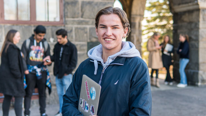 Elev med laptop foran skolebygningen